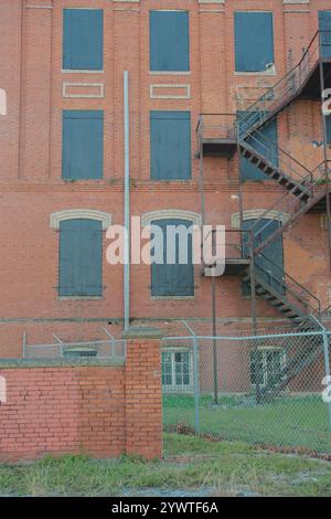 Lato della vecchia parete in muratura di mattoni rossi con sei finestre ad arco coperte nere. Un incendio metallico sfugge sulla destra. Barre di sicurezza in acciaio nero. Foto Stock