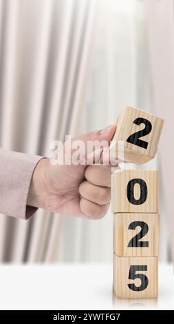 La mano d'affari costruisce una pila di cubi di legno con 2025 numeri sul tavolo. Happy New Year Concept o Celebration Foto Stock
