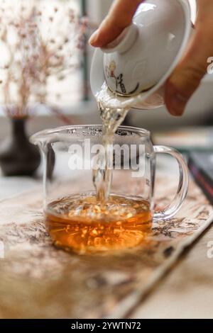 Versare una deliziosa e rilassante tazza di tè in una caraffa di vetro splendidamente realizzata porta gioia Foto Stock