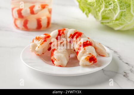 Gamberetti di surimi su un piatto su un piano di marmo. Gamberetti di surimi come ingrediente proteico per insalate e spuntini. Specialità di pesce, cucina giapponese e asiatica. Foto Stock