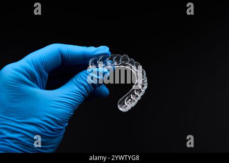 Una persona con guanti elettrici blu sta tenendo una protezione per la bocca trasparente, sottolineando con il proprio gesto liquidi, scienza e materiali in vetro Foto Stock
