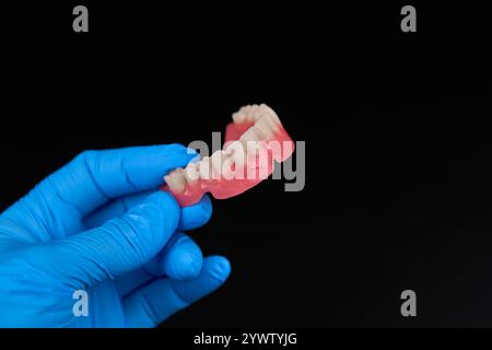 Nell'immagine, c'è un individuo con guanti blu che reggono una dentatura. L'attenzione è rivolta alla mano delle persone e alla dentatura che stanno tenendo Foto Stock