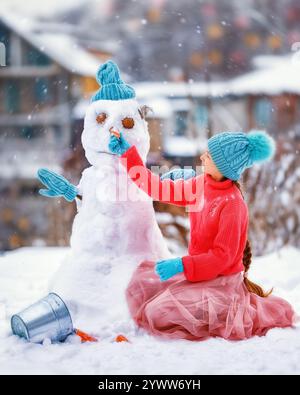 La ragazzina fa il pupazzo di neve in una giornata ghiacciata d'inverno. Il bambino fa il naso con la carota. Divertimento all'aperto per tutta la famiglia durante le vacanze natalizie nel Capodanno invernale Foto Stock