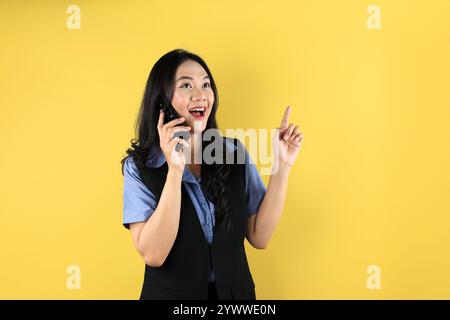 La giovane donna d'affari asiatica ha un'idea brillante durante una chiamata telefonica, isolata su sfondo giallo Foto Stock