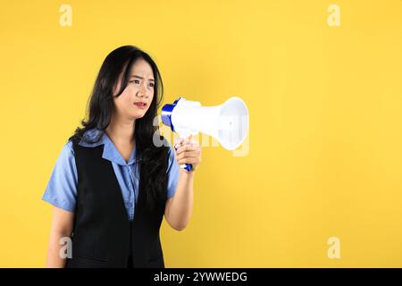 Sconvolta la giovane donna asiatica che tiene Un megafono, cercando di consegnare un messaggio di protesta, isolata su sfondo giallo Foto Stock