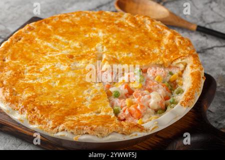 Pentola con pesce rosso, piselli verdi, carote, mais e salsa alla panna ricoperta di impasto croccante da primo piano in un piatto da forno sul tavolo. Orizzontale Foto Stock