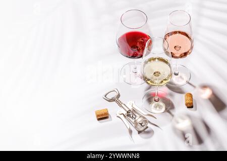 Tre bicchieri da vino pieni di vino rosso, bianco e rosa, in piedi graziosamente su uno sfondo luminoso e minimalista. Una vivace esposizione di varietà di vini Foto Stock