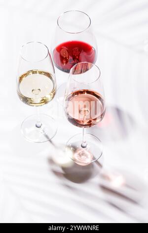 Tre bicchieri da vino pieni di vino rosso, bianco e rosa, in piedi graziosamente su uno sfondo luminoso e minimalista. Una vivace esposizione di varietà di vini Foto Stock