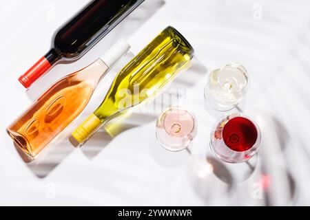 Tre bicchieri da vino pieni di vino rosso, bianco e rosa, in piedi graziosamente su uno sfondo luminoso e minimalista. Una vivace esposizione di varietà di vini Foto Stock