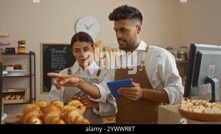 Uomo e donna che lavorano insieme in una panetteria, discutono di affari mentre sono circondati da prodotti da forno al coperto Foto Stock