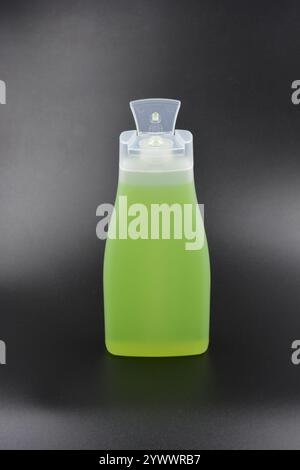 Flacone trasparente, bianco opaco con dispenser, prodotto cosmetico. Una bottiglia di plastica riempita con un liquido verde chiaro si trova su una plastica nera. Foto Stock