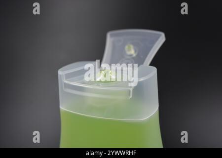 Flacone trasparente, bianco opaco con dispenser, prodotto cosmetico. Una bottiglia di plastica riempita con un liquido verde chiaro si trova su una plastica nera. Foto Stock