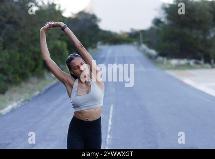 Una giovane donna snella indossa un abbigliamento fitness che riscalda le mani mentre cammina su una strada abbandonata Foto Stock