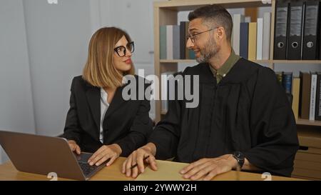 Donna e uomo che lavorano insieme in un ufficio, con l'uomo vestito da giudice e la donna come avvocato, che discute di questioni legali. Foto Stock