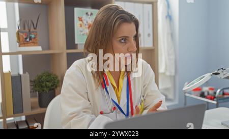 Una bella donna bionda veterinaria in una stanza clinica con indosso un cappotto bianco e uno stetoscopio, concentrata sul suo lavoro nel posto di lavoro veterinario al chiuso. Foto Stock