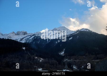 Una vista panoramica delle cime innevate dei Pirenei. Il primo piano mostra un'area boschiva con un mix di alberi sempreverdi e decidui. Una strada e infr Foto Stock