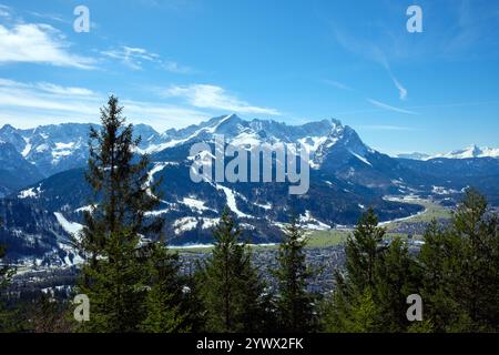 Questo paesaggio invernale mostra le maestose montagne che circondano Garmisch-Partenkirchen. Gli alberi di pino incorniciano la vista sotto un cielo blu limpido Foto Stock