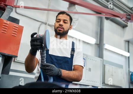 Il giovane meccanico si concentra intensamente mentre lavora su un veicolo in un garage moderno. Foto Stock