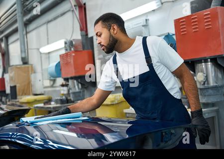 Il giovane meccanico si concentra con attenzione sulla lucidatura della superficie di un'auto in un'officina. Foto Stock