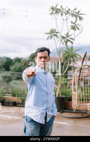 Un uomo del sud-est asiatico che mostra frustrazione, punta in avanti con un'espressione intensa, cattura un'emozione di rabbia o disaccordo. Foto Stock