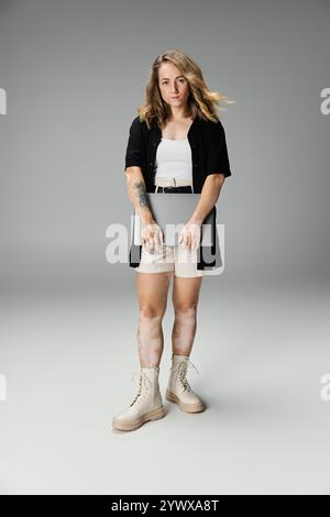 Una giovane donna con vitiligine mette in mostra la sua bellezza con un notebook su uno sfondo grigio. Foto Stock