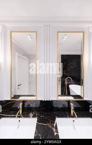 Un bagno con marmo e piastrelle verticali sovrapposte della metropolitana, un mobile vanity bianco in quercia, specchi e rubinetti quadrati con cornice nera e ripiano in marmo. Foto Stock