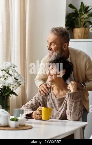 Una coppia allegra si rilassa a casa, condividendo sorrisi e calore sul caffè in un ambiente accogliente. Foto Stock