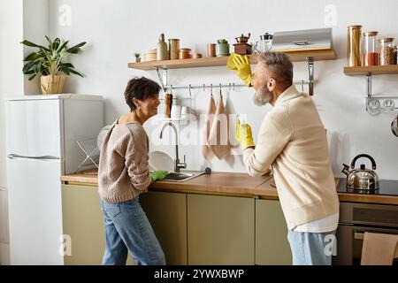 Una coppia felice si impegna in un momento divertente mentre si lava i piatti nella loro accogliente cucina. Foto Stock