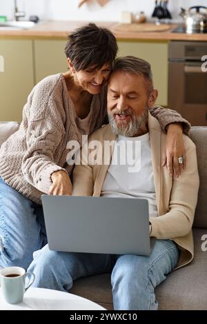 Una coppia di anziani felice condivide le Risate e l'amore mentre naviga online dal loro comodo divano. Foto Stock