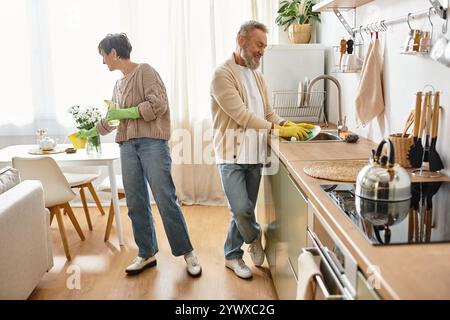 Una coppia matura condivide momenti di gioia mentre lavano i piatti nella loro calda cucina. Foto Stock