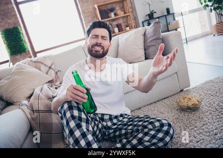 Foto di un giovane barbuto triste e attraente in pigiama nel weekend a casa a guardare le partite di calcio che falliscono al chiuso Foto Stock