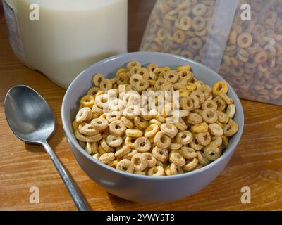 Primo piano di cereali secchi in una confezione e in una ciotola per la colazione, accanto a un cucchiaio e a una scatola di latte. Foto Stock
