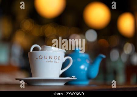 Primo piano di una teiera e di una tazza di latte sul tavolo del ristorante con una leggera illuminazione sullo sfondo. Foto Stock