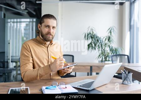 Giovane professionista che prende appunti alla sua scrivania, incarna produttività e concentrazione in un ambiente di lavoro. Foto Stock