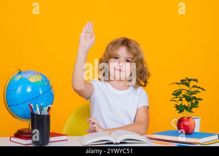 Bambino della scuola che alza la mano, disposto a rispondere alle domande. Il ragazzo della scuola nerd isolato sullo sfondo dello studio. Bambino intelligente della scuola elementare con il libro. Foto Stock