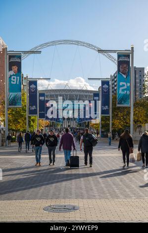 Persone che passano attraverso Olympic Way, una via pedonale di negozi ristoranti e luoghi di intrattenimento, lo stadio di Wembley, sullo sfondo del Regno Unito Foto Stock