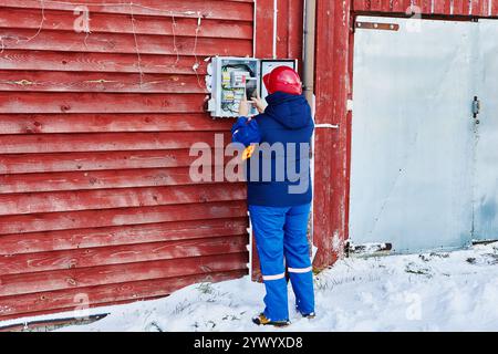 Uno specialista di una società di fornitura di energia ispeziona le apparecchiature elettriche all'aperto della famiglia in inverno. Foto Stock