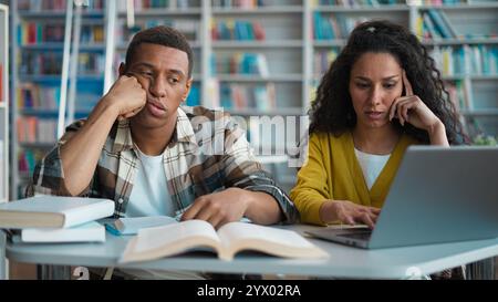 Studenti stanchi uomo afroamericano donna latina araba team di progetto biblioteca stanchi compagni di classe assonnati studenti universitari che imparano a preparare lo studio Foto Stock