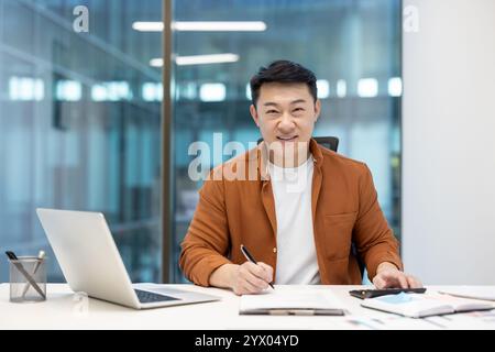Uomo asiatico, uomo d'affari maturo che lavora alla sua scrivania, usando il computer portatile e gli appunti. Foto Stock