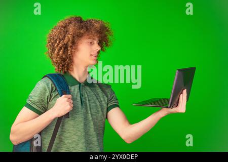 La Chroma Key verde brillante rappresenta il palcoscenico per l'uomo dai capelli ricci, che mostra con sicurezza il suo laptop, indossato con una camicia. Foto Stock