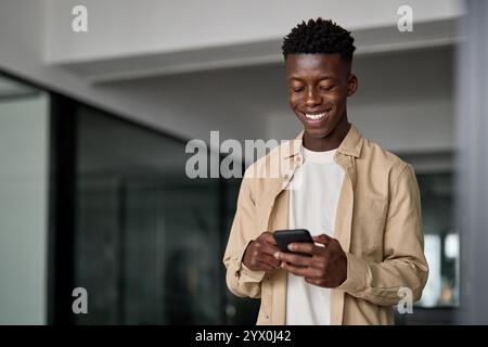 Felice uomo d'affari africano che usa lo smartphone in piedi al lavoro in ufficio. Foto Stock