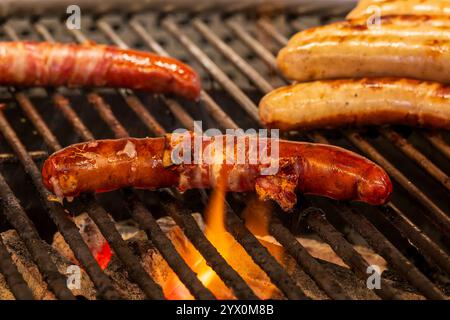 Le salsicce cucinano su un grill su una fiamma ardente e carboni caldi. Foto Stock