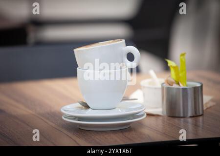 Due tazze da caffè impilate poggiano su un tavolino da caffè, macchie sottili che suggeriscono i sorsi più recenti. La scena suggerisce la cultura del caffè di tutti i giorni e il calore sociale i Foto Stock