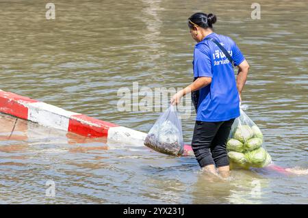 SAMUT PRAKAN, THAILANDIA, 19 novembre 2024, Una donna con passeggiate per lo shopping attraverso strade allagate Foto Stock