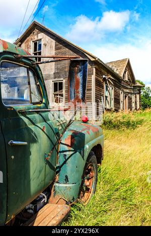 Un vecchio camion verde è parcheggiato davanti a una casa. La casa è vecchia e malandata, con molta ruggine. Il carrello è parcheggiato davanti alla casa, Foto Stock