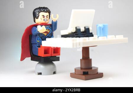 LEGO Superman frustrato lavorando da casa sul suo laptop, con Una tazza di caffè sulla sua scrivania. Foto Stock