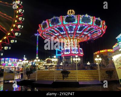 Kettenkarussell. Ein Regentag auf dem Winterdom. Kaum Besucher, dafür spiegeln sich die Lichter auf dem nassen Pflaster. Amburgo amburgo 2024 - inverno 08 *** carosello a catena Una giornata di pioggia al Winter Dome quasi nessun visitatore, ma le luci si riflettono sul marciapiede bagnato amburgo 2024 inverno 08 Foto Stock