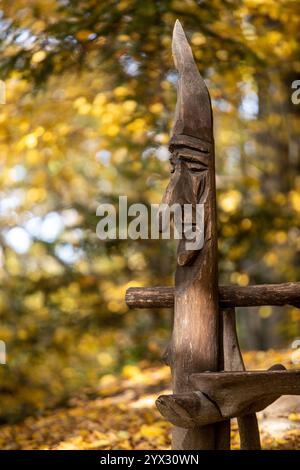 una testa scolpita in legno da un artista sconosciuto sullo sfondo di una foresta dai colori autunnali Foto Stock