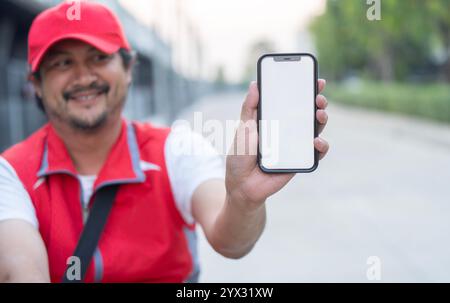 Un uomo asiatico con una buona consegna è seduto su una bicicletta e mostra uno smartphone con schermo vuoto. Attenzione selettiva al telefono. Foto Stock