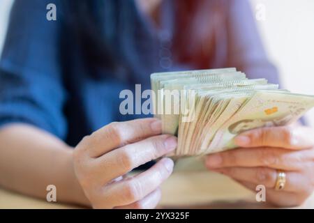 La donna prende una banconota da un pacchetto di 20 banconote thailandesi su sfondo bianco. Donna che tiene in mano i soldi thailandesi. Vista ravvicinata. Foto Stock
